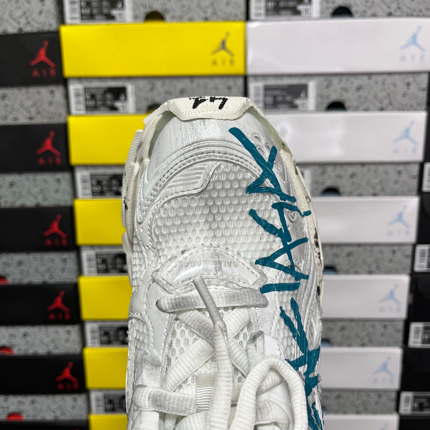 White sneaker heel with teal-blue branding and textured upper panels.