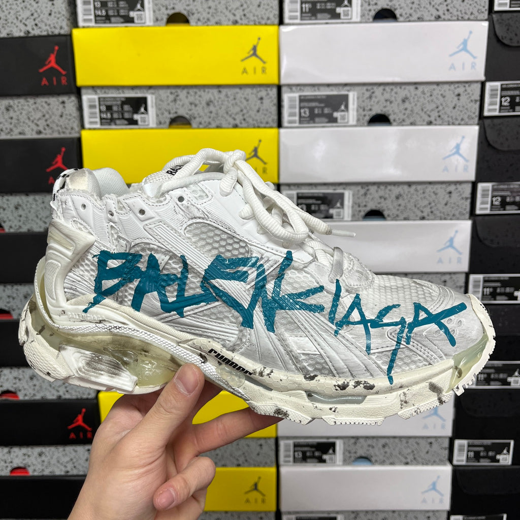 White sneaker with teal-blue side logo graphic and lace-up front.