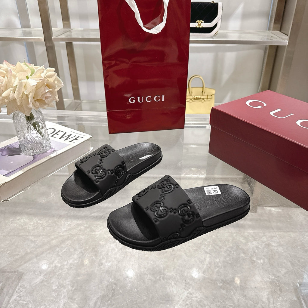 Black slide sandals with embossed GG logo on the front strap and wide footbed