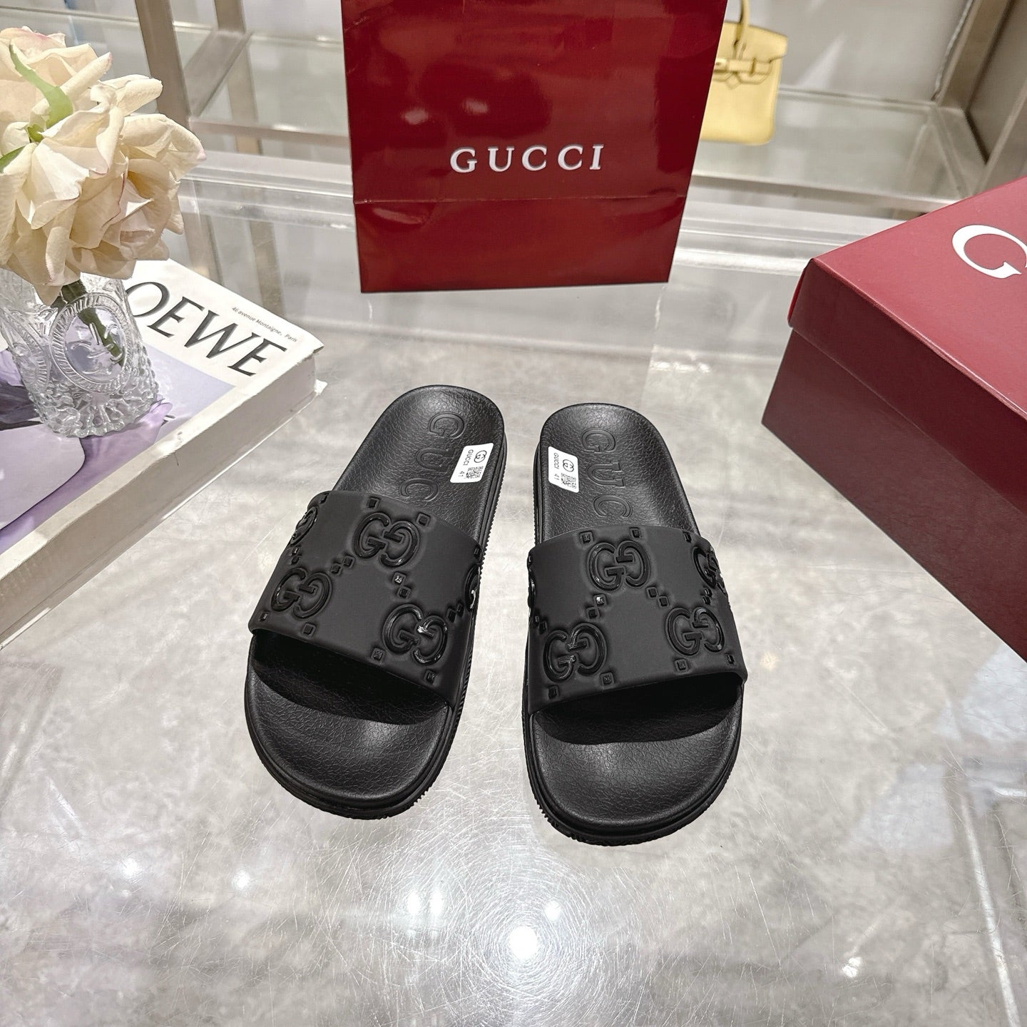 Black slide sandals with textured GG logo embossing on two straps, pair view