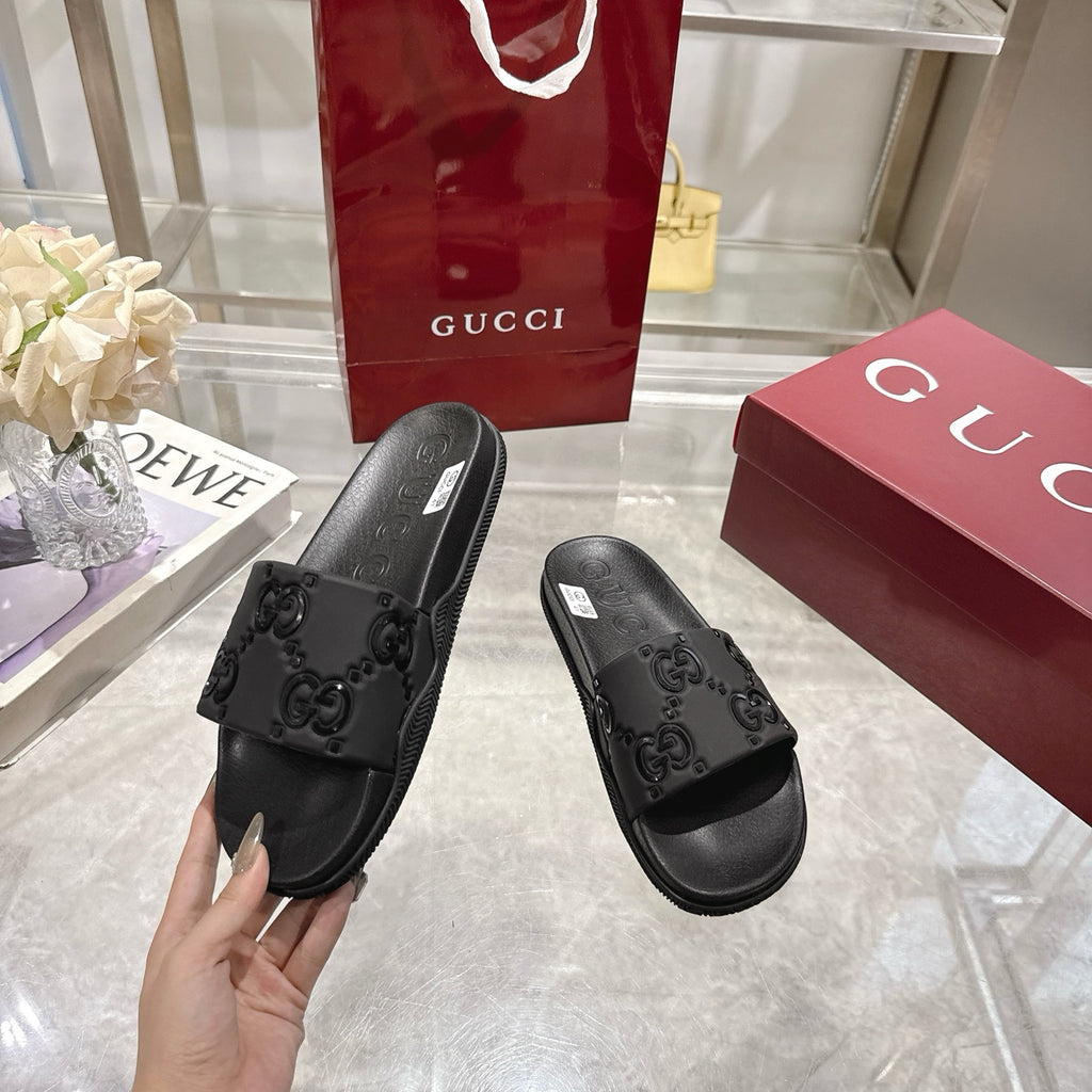 Black Gucci slide sandals held by the heel and toe, embossed GG pattern on strap