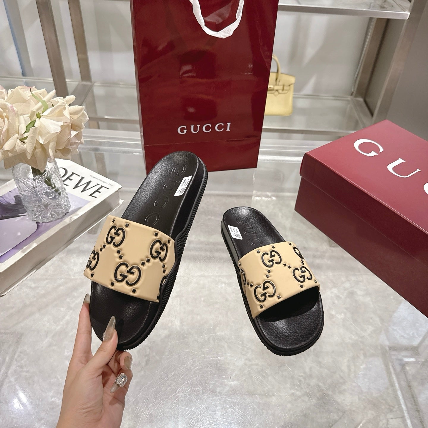 Black and beige GG slide sandals, shown being held by the heel
