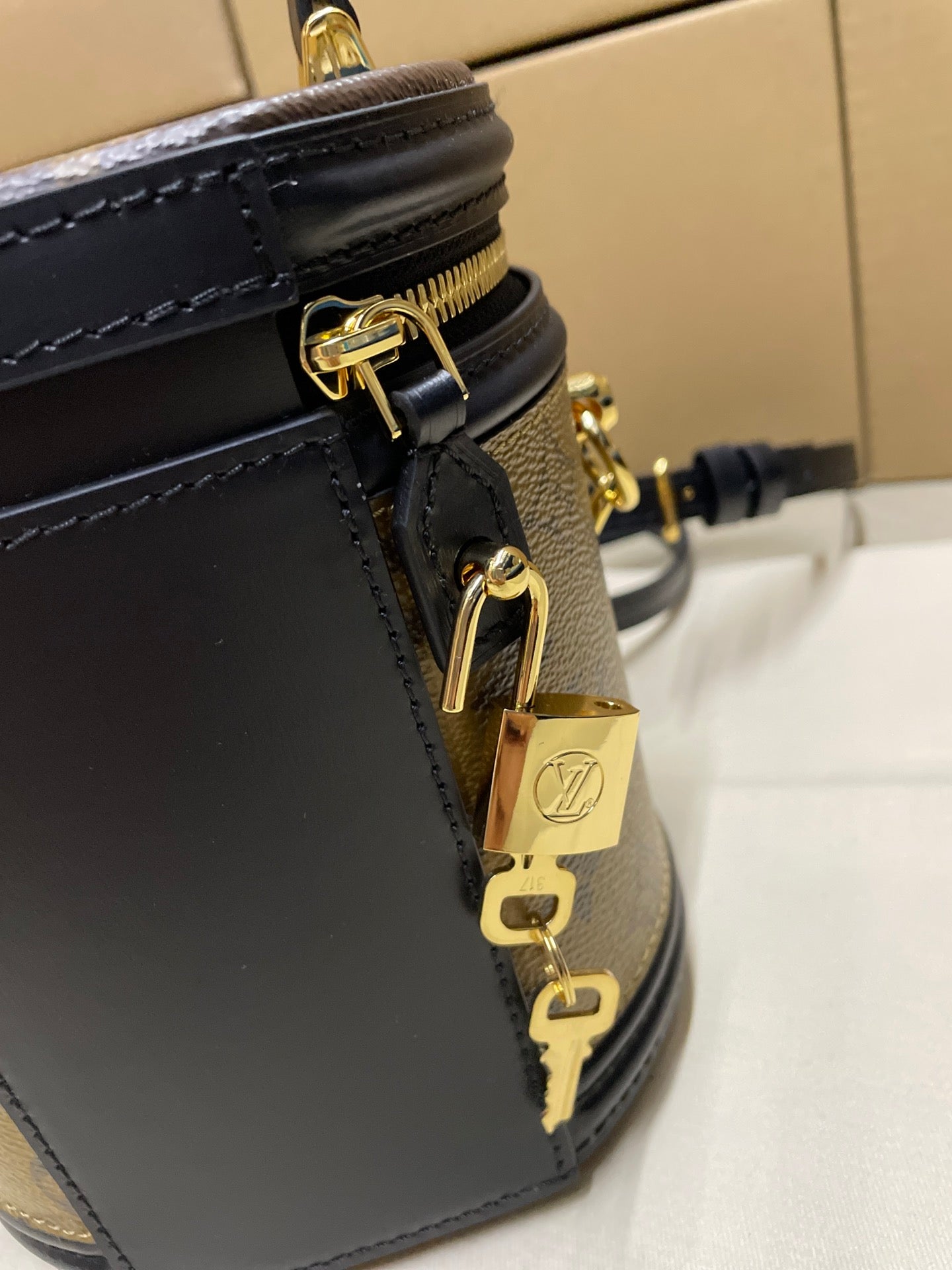 Louis Vuitton bag close-up of black leather strap attachment with gold hardware and lock charm