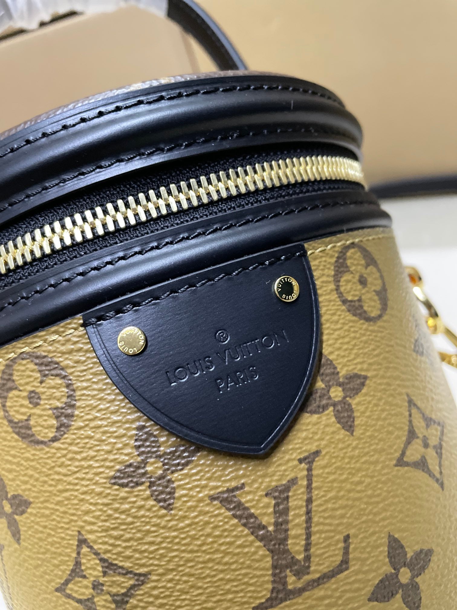 Louis Vuitton bag close-up of black leather trim with gold zipper hardware and logo patch