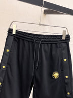 Black drawstring track pants with gold emblem patches and round front badge