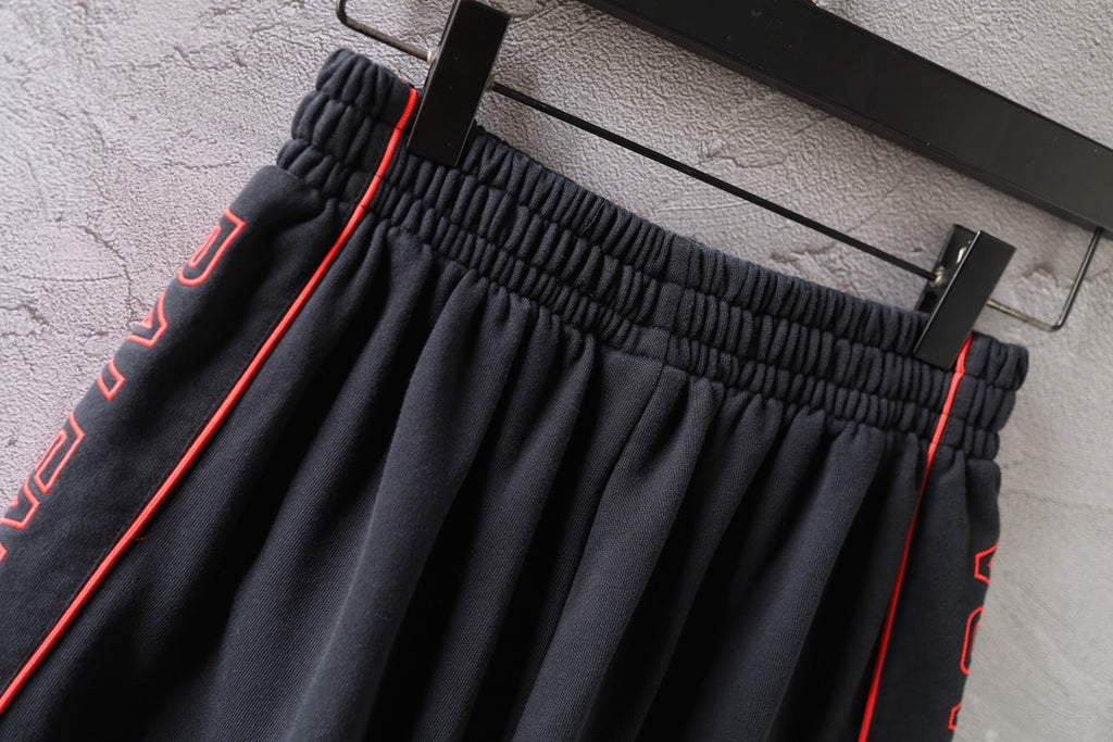 Black Balenciaga shorts waistband close-up with red-trimmed side stripes and pleats.