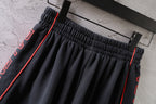 Black Balenciaga shorts waistband close-up with red-trimmed side stripes and pleats.