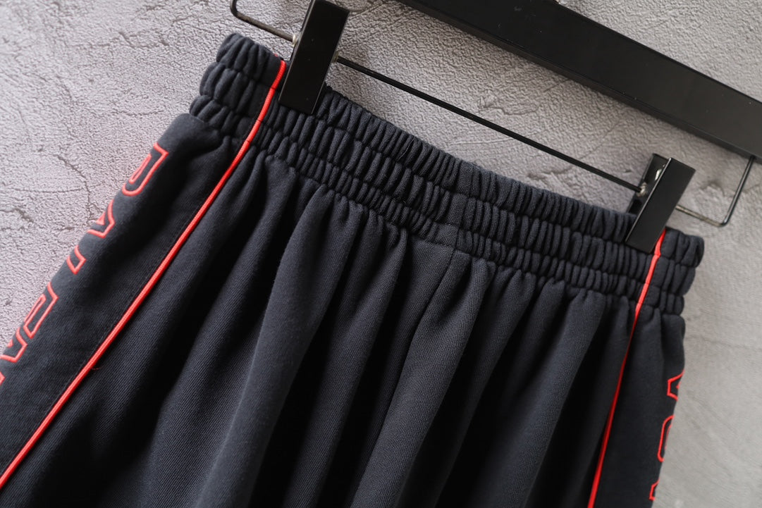 Black Balenciaga shorts waistband close-up with red-trimmed side stripes and pleats.