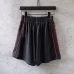 Black Balenciaga shorts with red-trimmed sides and pleated front, elastic waist.