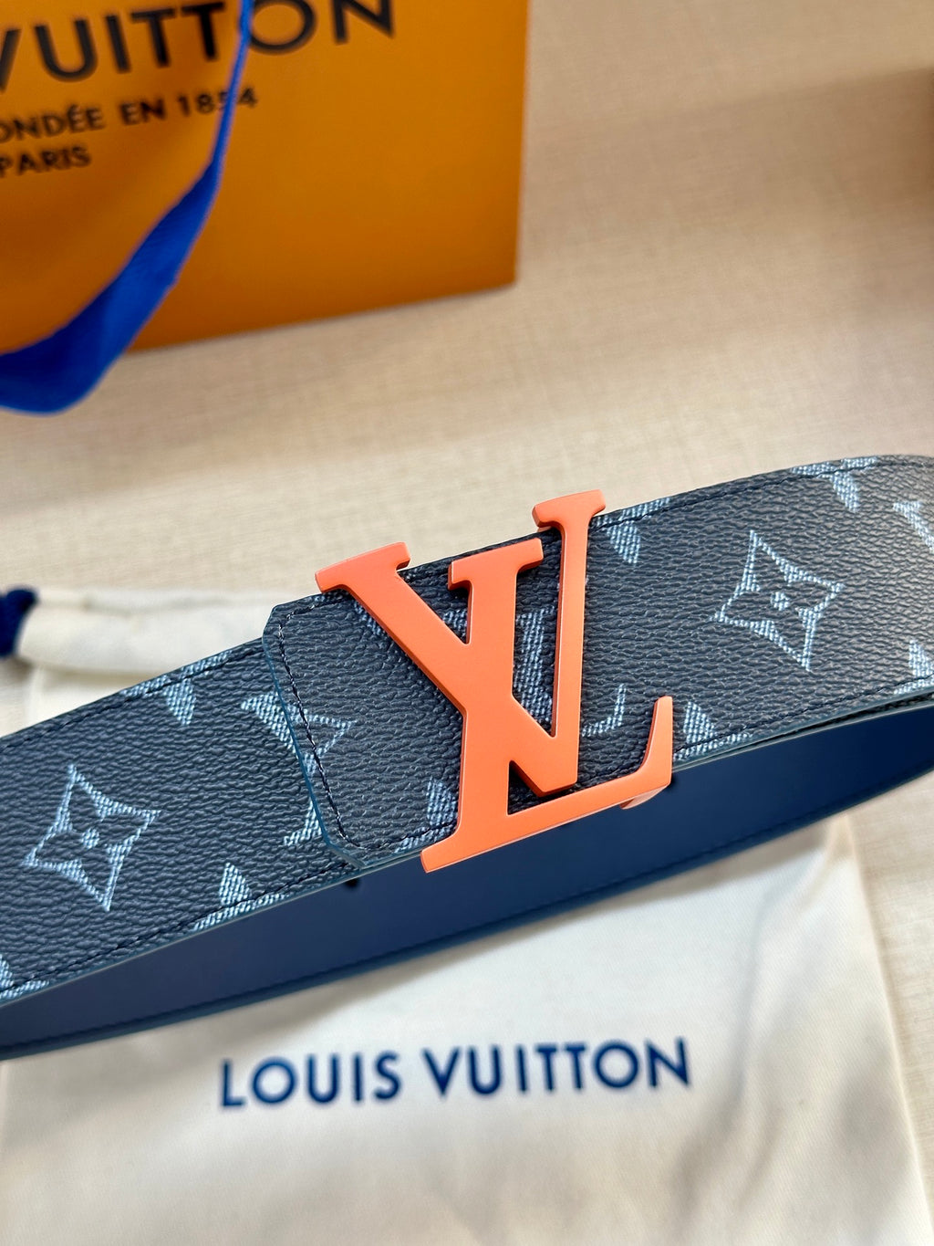 Louis Vuitton belt close-up with dark blue strap and orange LV buckle