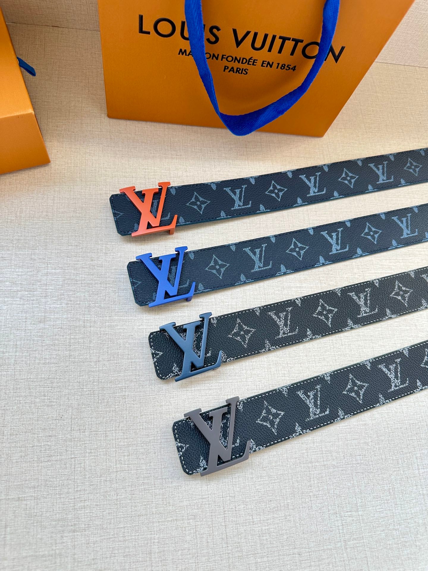 Louis Vuitton monogram belts in dark blue with orange LV buckles, laid out