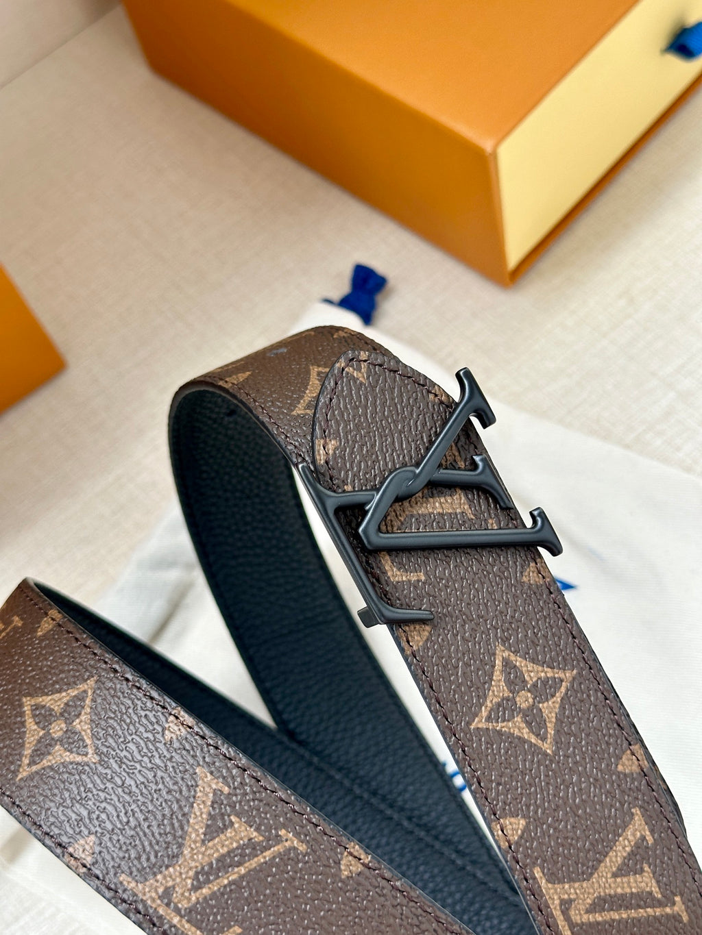 Louis Vuitton monogram belt buckle detail with dark leather strap and V metal clasp