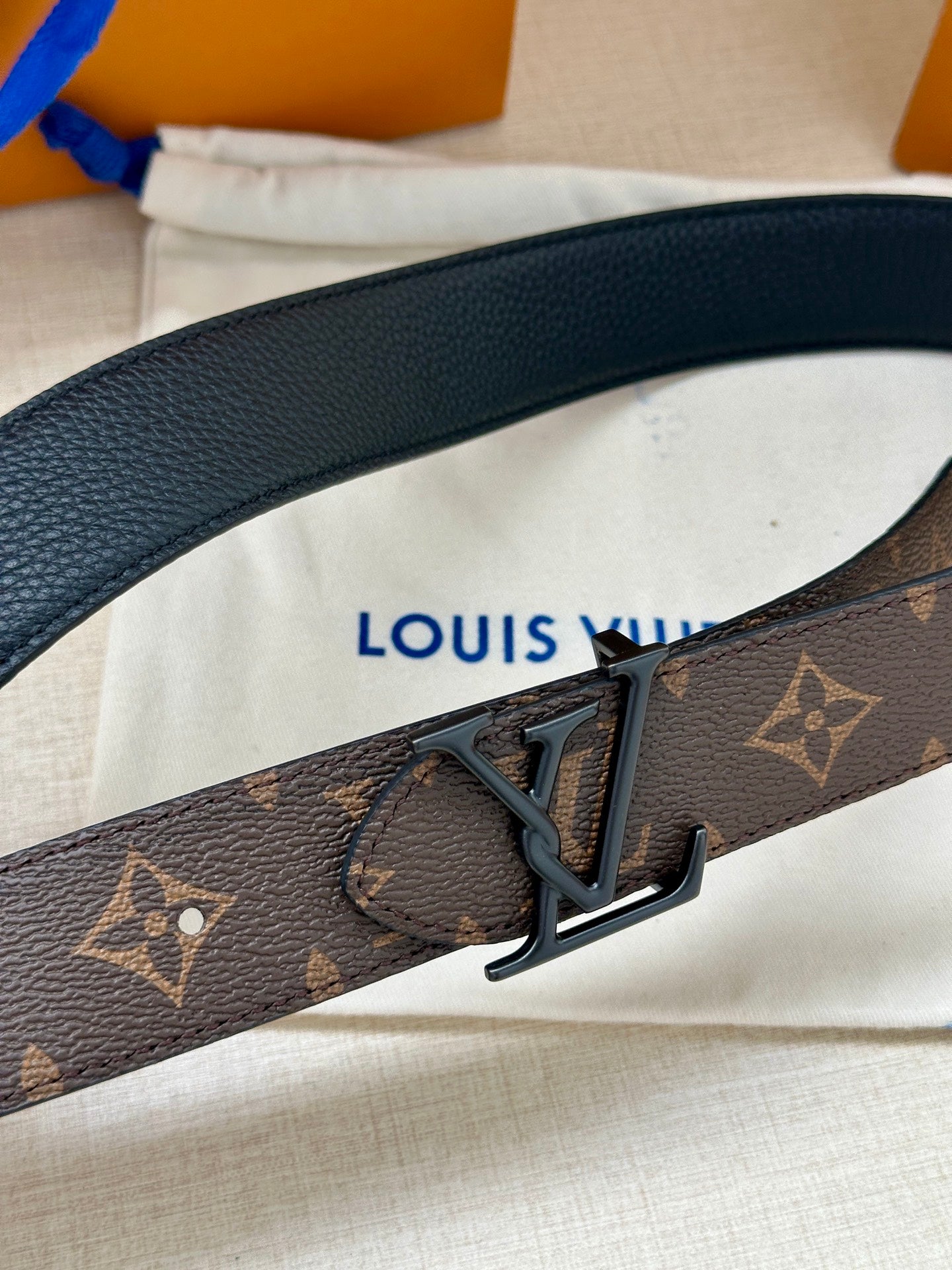 Louis Vuitton monogram belt close-up with dark V metal buckle and leather keeper