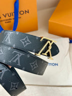 Louis Vuitton monogram belt close-up with gold-tone LV buckle, dark navy repeating pattern.