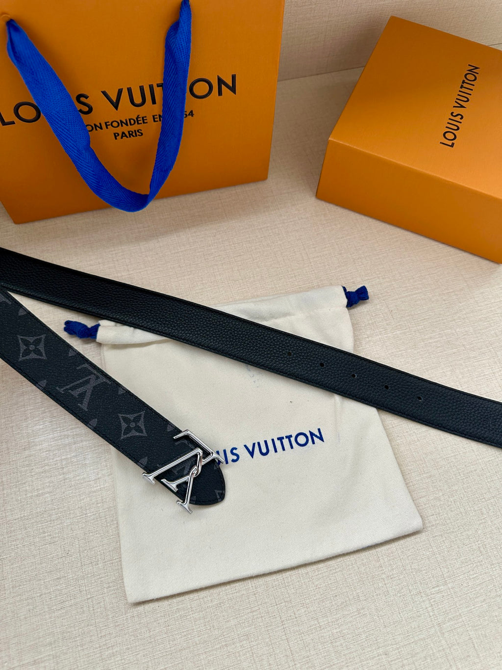Louis Vuitton monogram belt laid flat with silver-tone LV buckle, dark navy logos.