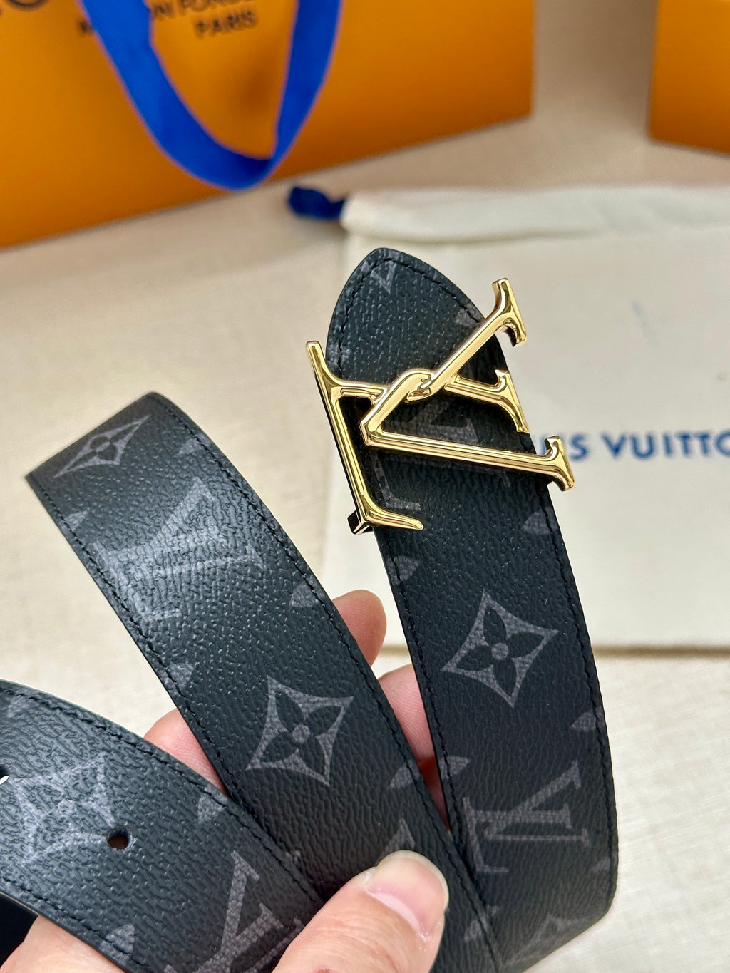 Louis Vuitton monogram belt close-up with gold-tone buckle, dark navy repeating logos.