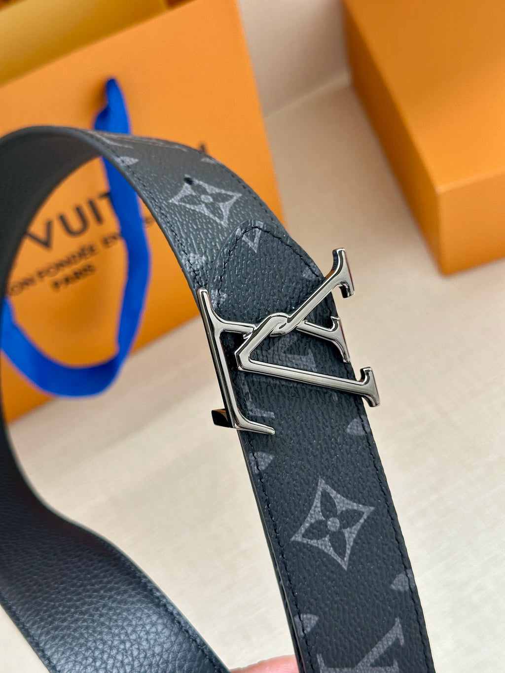 Louis Vuitton monogram belt close-up with silver-tone buckle and dark navy pattern.