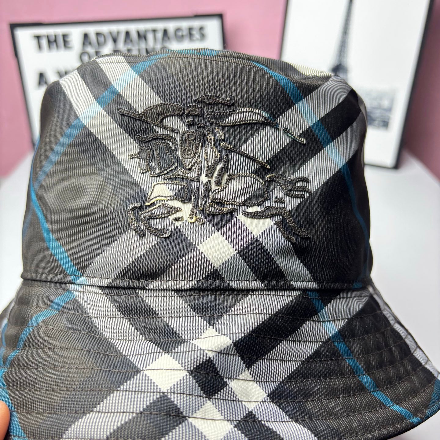 Embroidered crest detail on plaid bucket hat; black, white, and blue check pattern