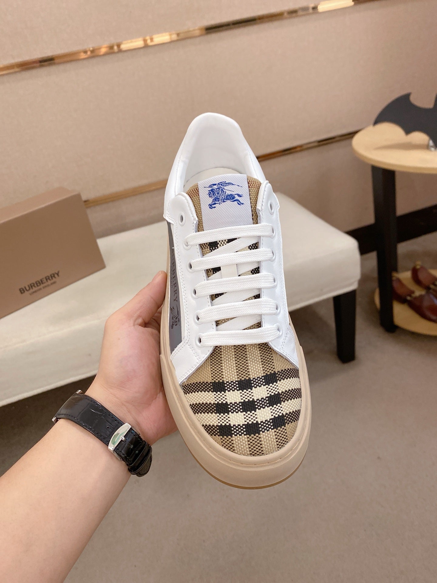 White low-top sneakers with plaid side stripe, blue logo patch, and rubber sole