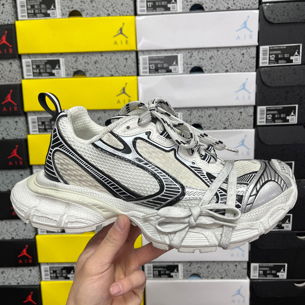 White Balenciaga sneakers with black trim, mesh panels, lace-up front, chunky sole.