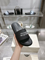 Black Alexander McQUEEN slide sandal with wide logo strap, held in hand