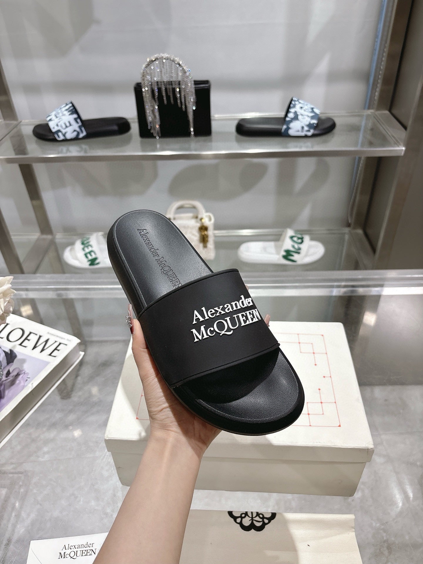 Black Alexander McQUEEN slide sandal with wide logo strap, held in hand