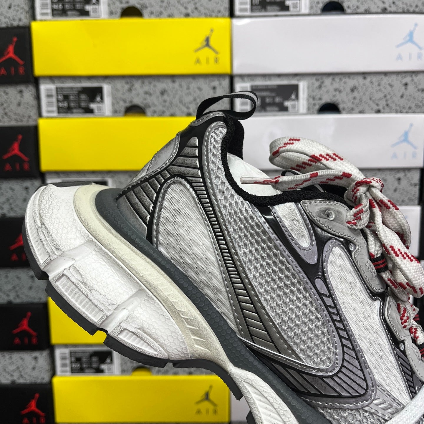 Sneaker side view with white laces, grey mesh, black overlays, and off-white sole