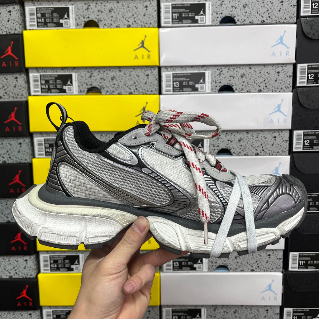 Chunky sneaker held up, grey mesh upper with white laces and red-and-black lace accents