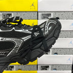 Black sneaker side view with white stripe detailing and chunky rubber sole