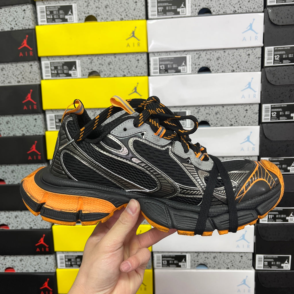 Front three-quarter view of black and silver sneaker with orange outsole and laces