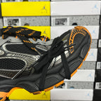 Side view of black and silver lace-up sneaker with orange edge detailing