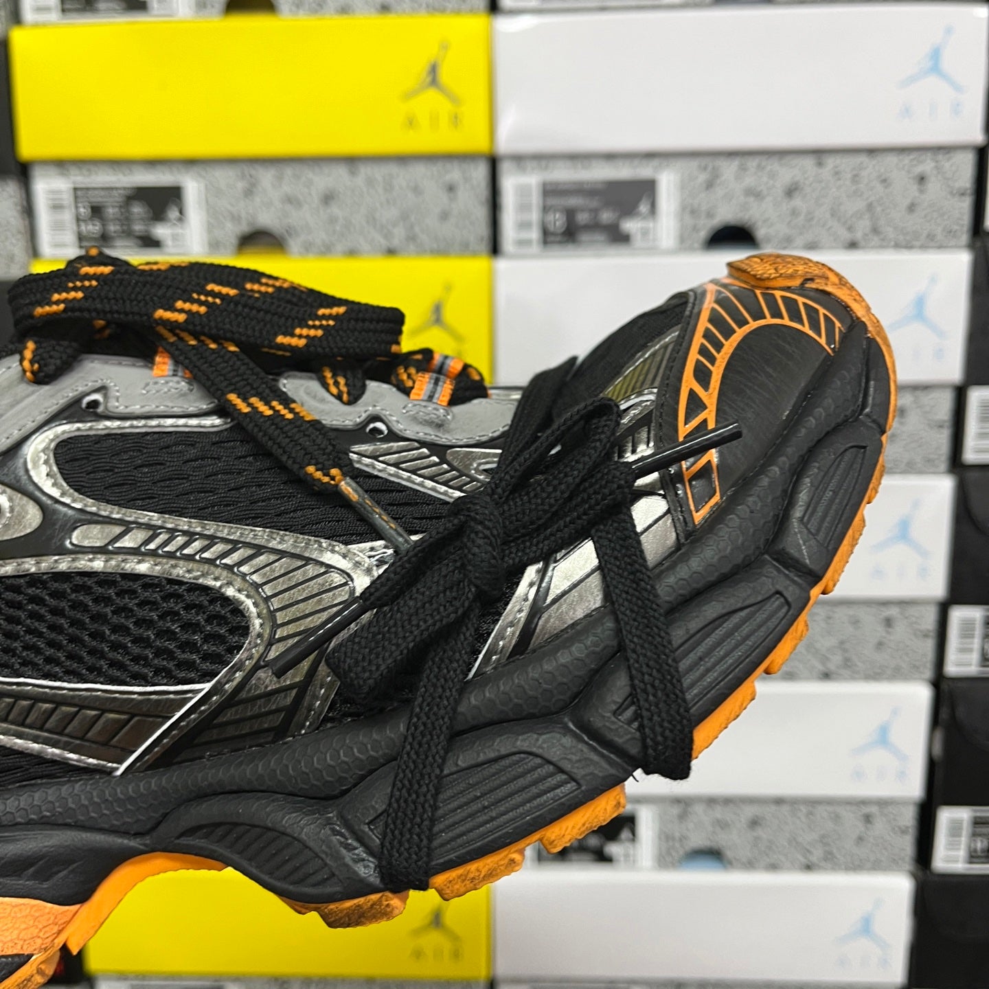 Side view of black and silver lace-up sneaker with orange edge detailing