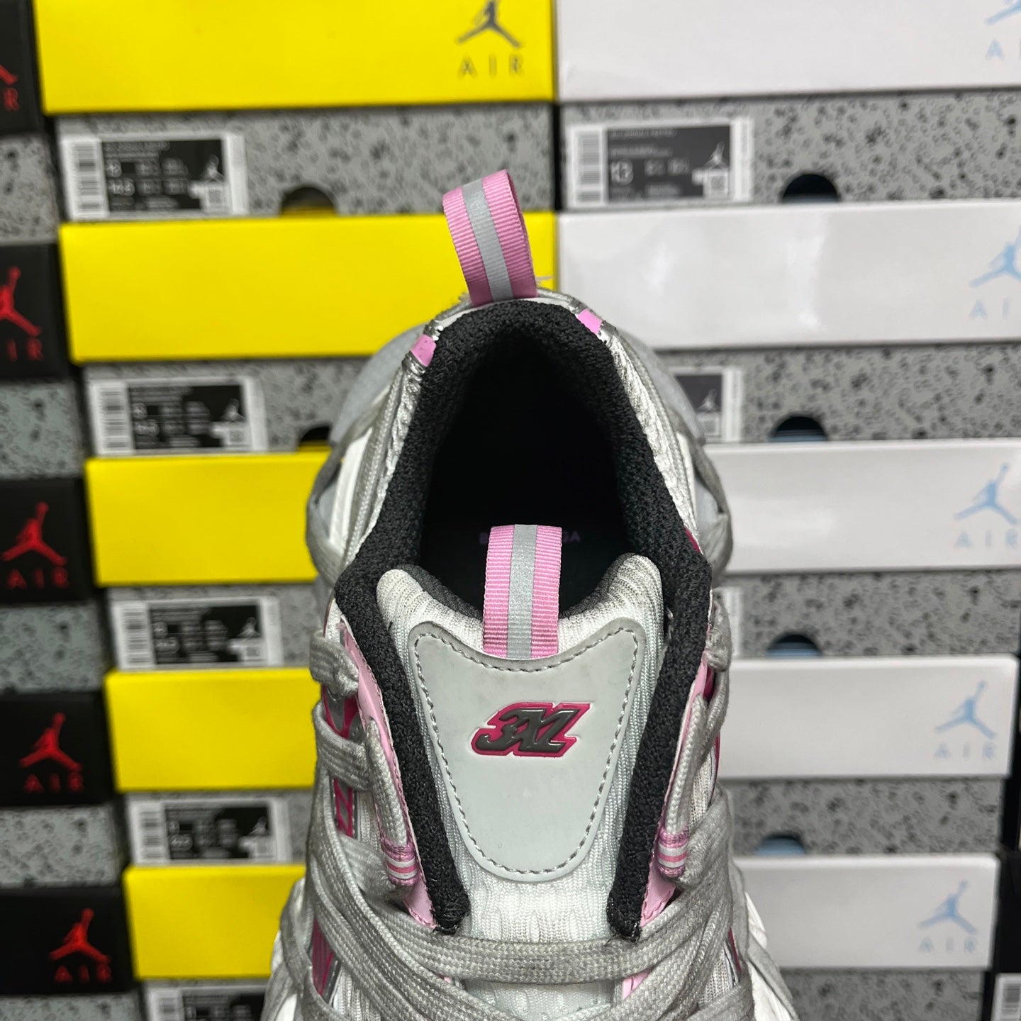 Light gray sneaker back view with pink strap and heel logo patch
