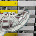 Side view of white lace-up sneaker with red striped overlays and light blue outsole edge
