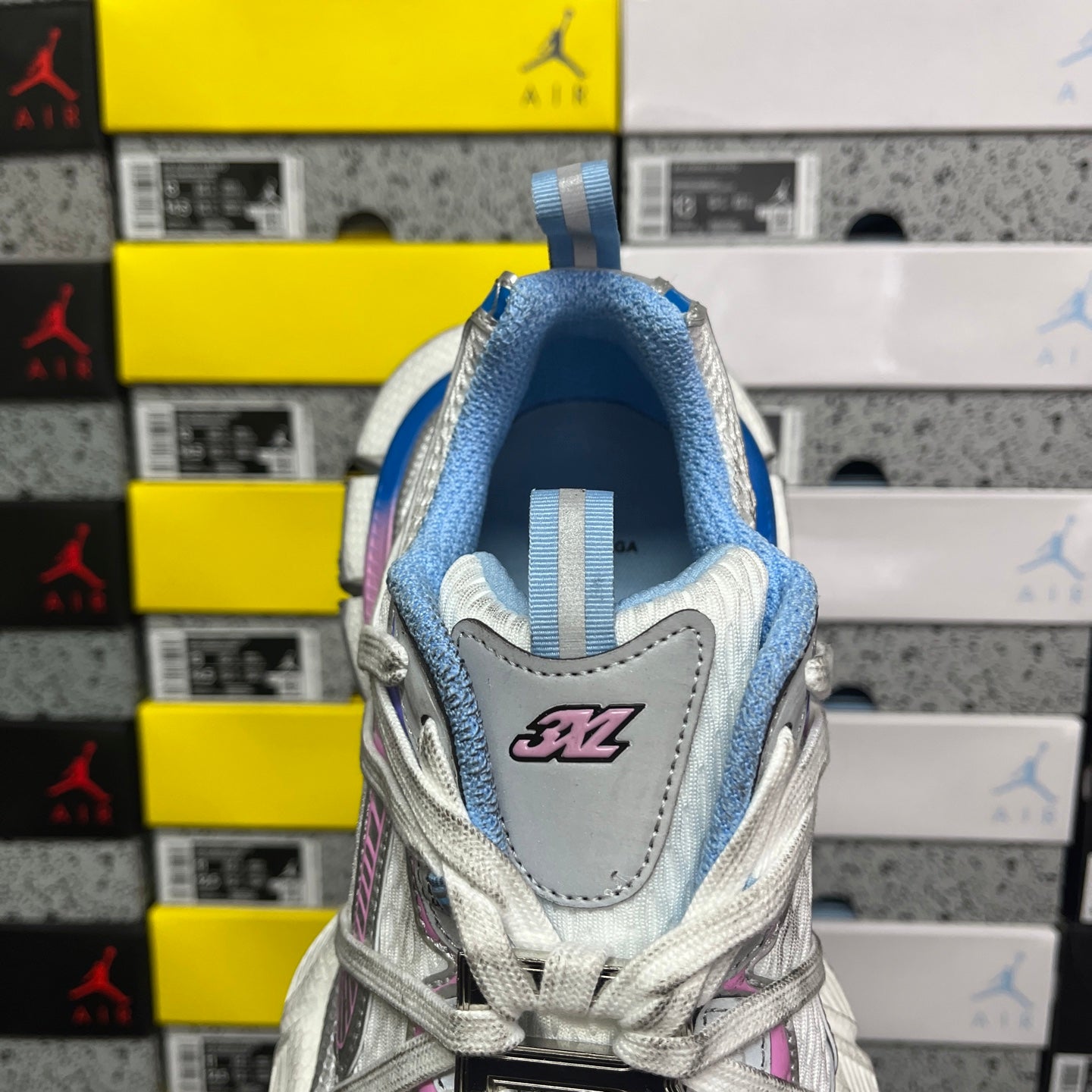 Rear view lace-up sneaker with light gray upper, blue collar, and stitched “3XL” logo