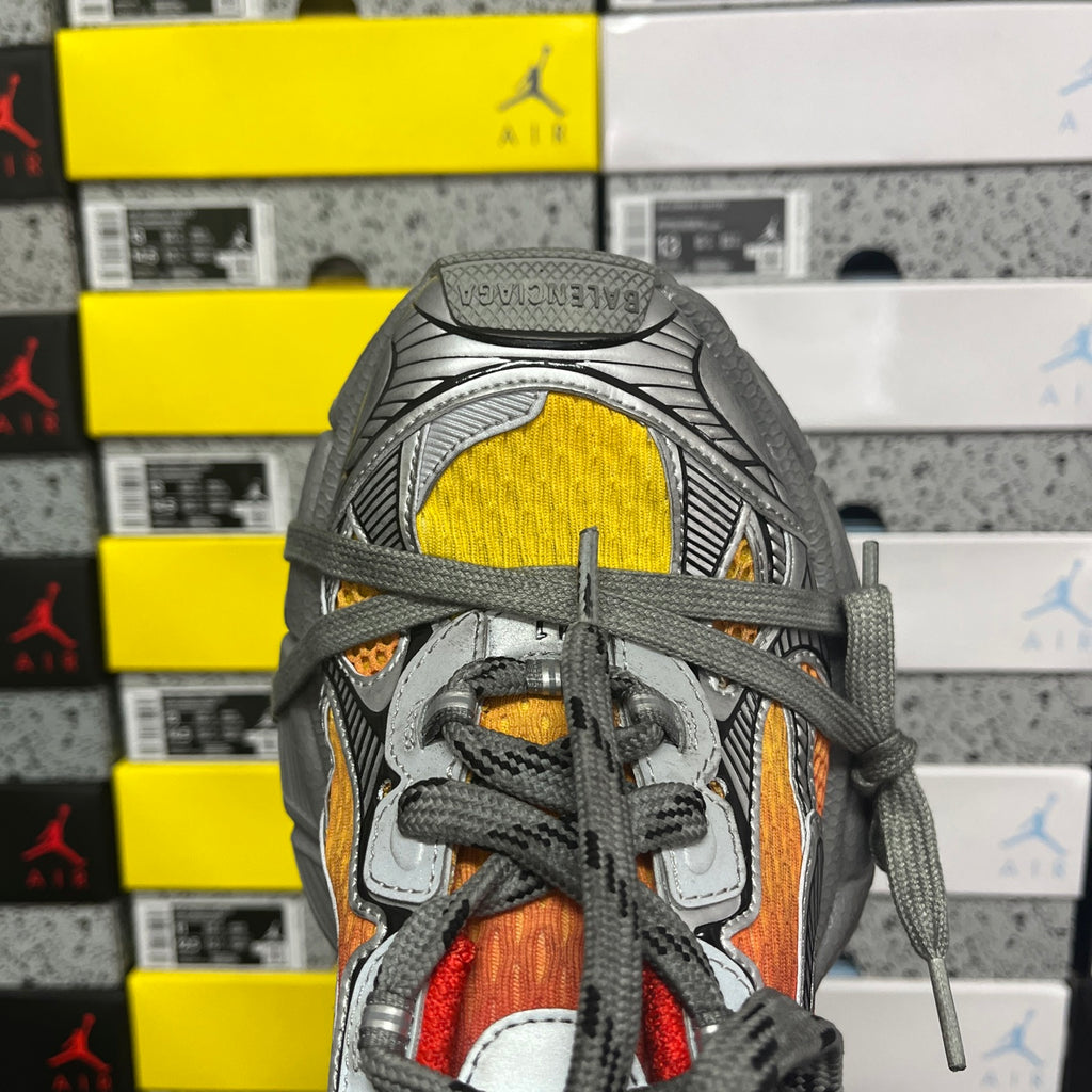 Sneaker toe and laces with red, orange, and yellow panels on a gray upper