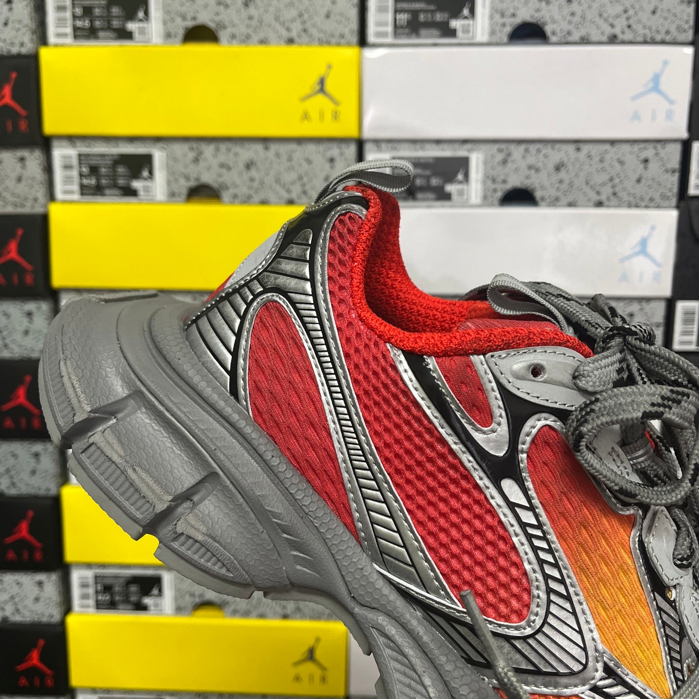 Sneaker quarter view: red mesh upper with gray overlays and black laces