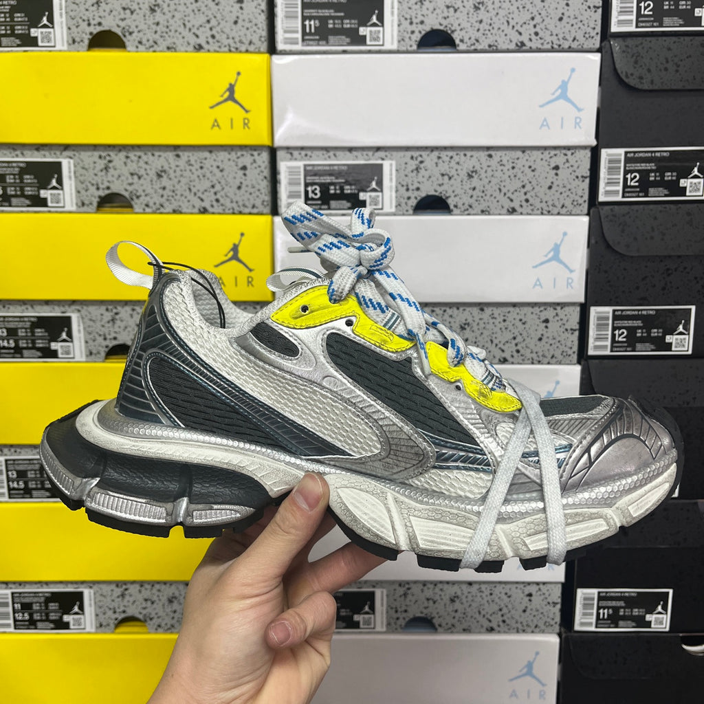 Grey and black running sneaker with neon yellow accent and blue striped laces, front view