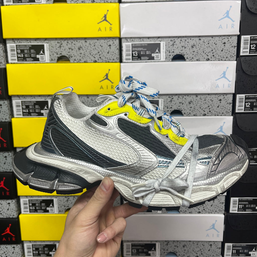 Grey, black and white running sneaker with neon yellow logo and blue striped laces