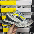 Grey, black and white running sneaker with neon yellow logo and blue striped laces