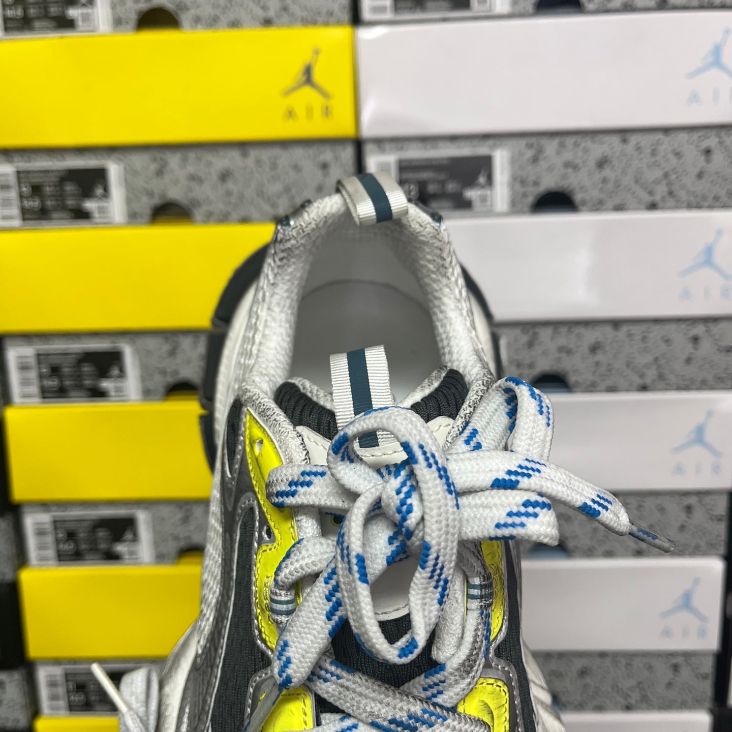 Grey sneaker with blue striped laces and neon yellow eyelet, tongue and collar close-up