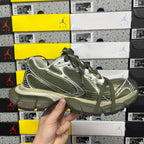 Green and silver sport sneakers with laces, held up against stacked shoe boxes