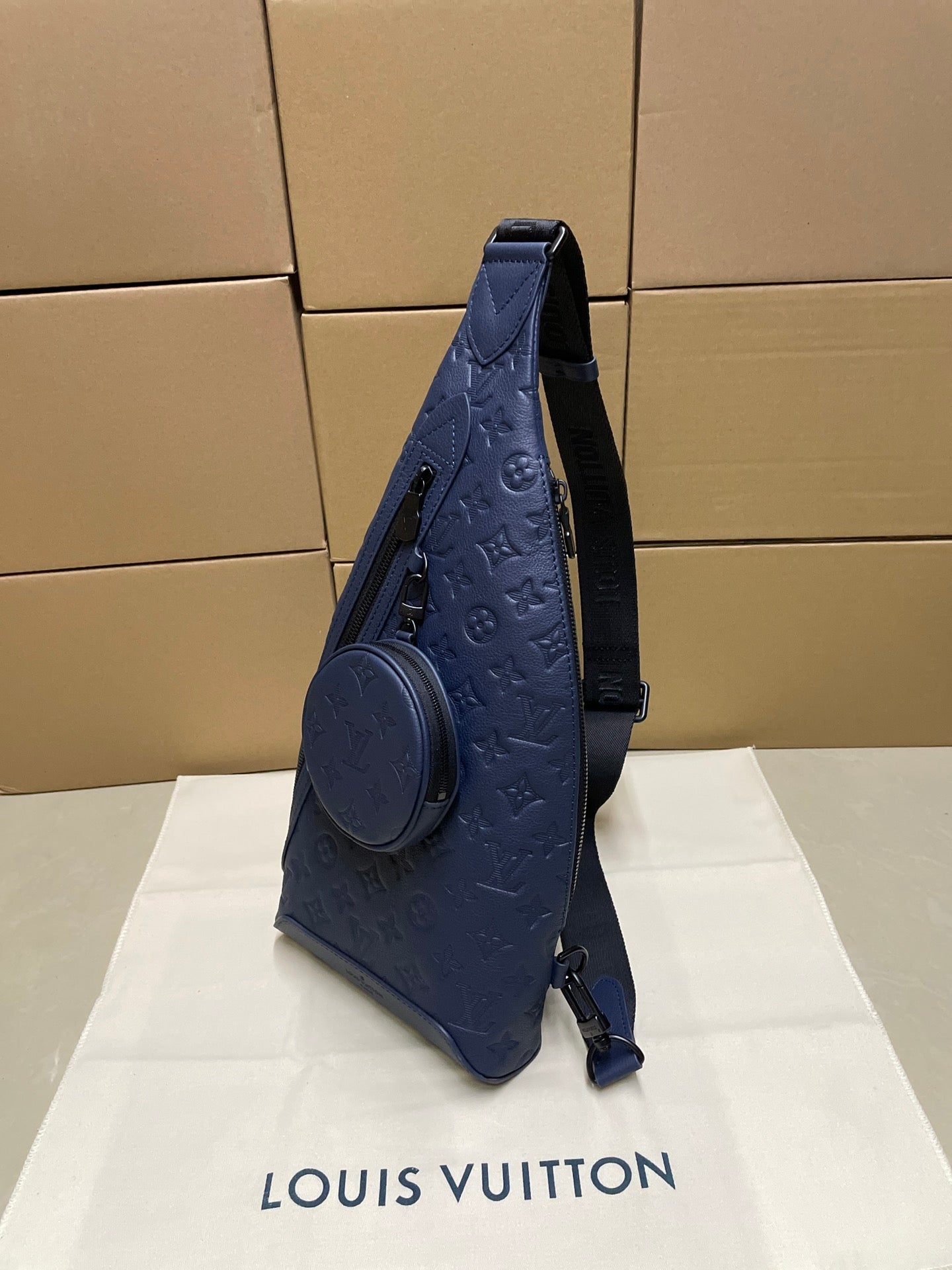 Blue monogram sling bag with two straps and round front pocket, side view