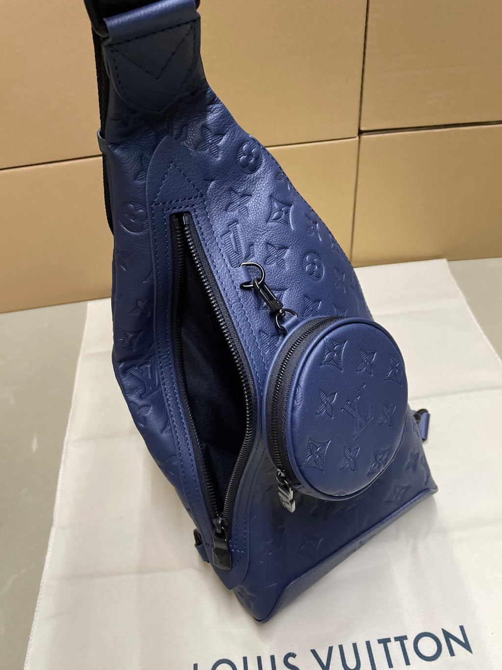 Dark blue monogram sling bag side view with zip closure and round front patch