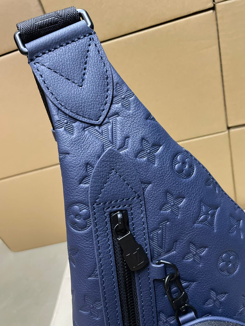 Dark blue monogram sling bag close-up with top strap tab and zip pocket