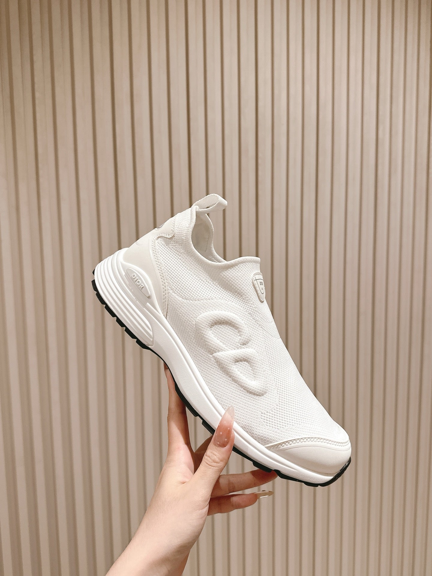 White slip-on sneaker held in hand, side profile with Dior logo detail