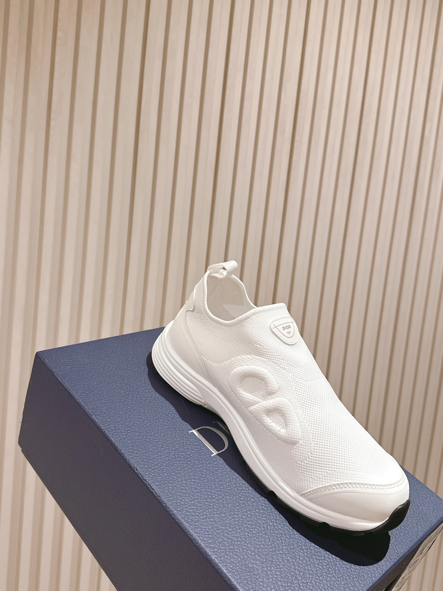 White slip-on sneaker on a blue box, side view with chunky sole and Dior logo