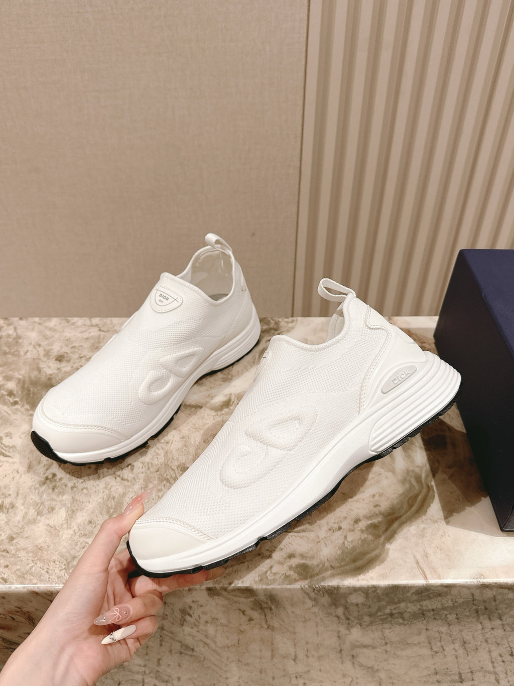 White slip-on sneakers with textured upper, shown from the side while held