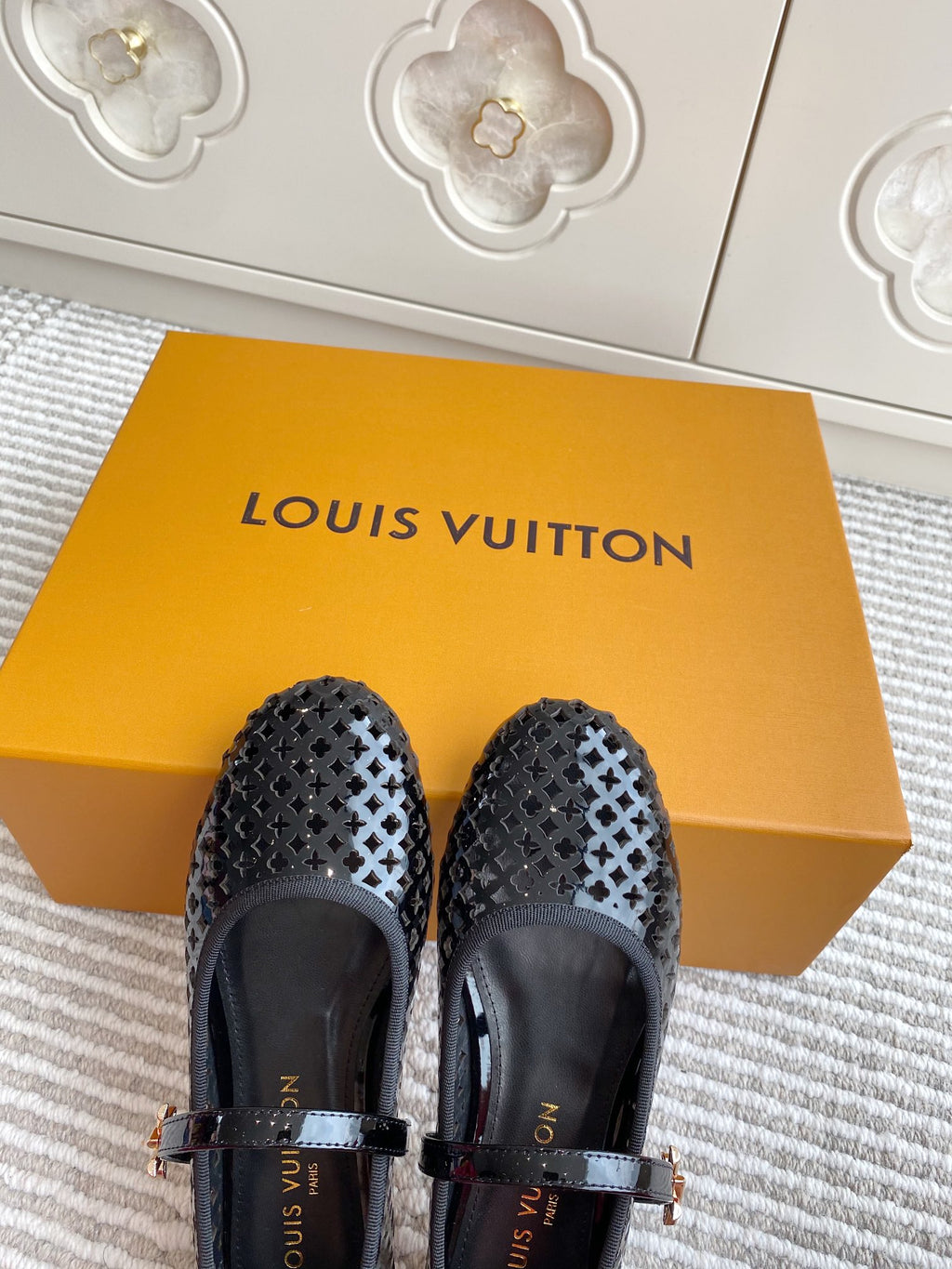 Black patterned flat ballerina shoes with buckle straps, front view on box