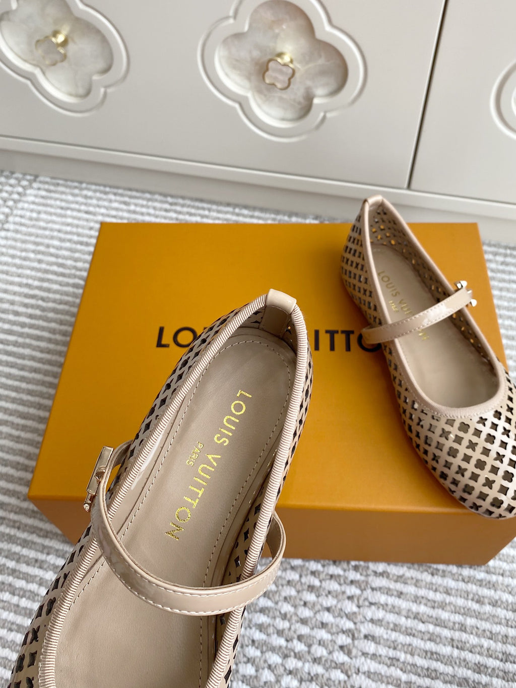 Women’s Louis Vuitton monogram flats angled view, cream patterned upper, adjustable strap and buckle.